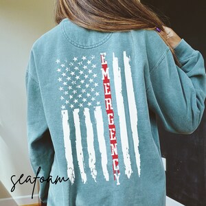 May include: Seafoam green sweatshirt with a distressed white American flag design and the word "EMERGENCY" in red down the center.