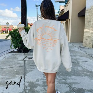 May include: A beige sweatshirt with an orange graphic of a sunset over the ocean and the text "sunset wanderer".