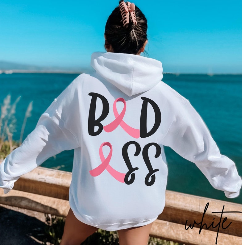 May include: White hoodie with a pink ribbon and the text "BADASS" printed on the back.