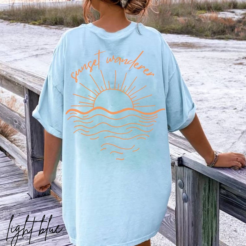 May include: Light blue t-shirt with a graphic of a sunset over the ocean and the text "sunset wanderer".
