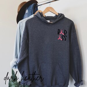 May include: Dark heather grey hooded sweatshirt with a pink ribbon and the text "B&D" on the front.