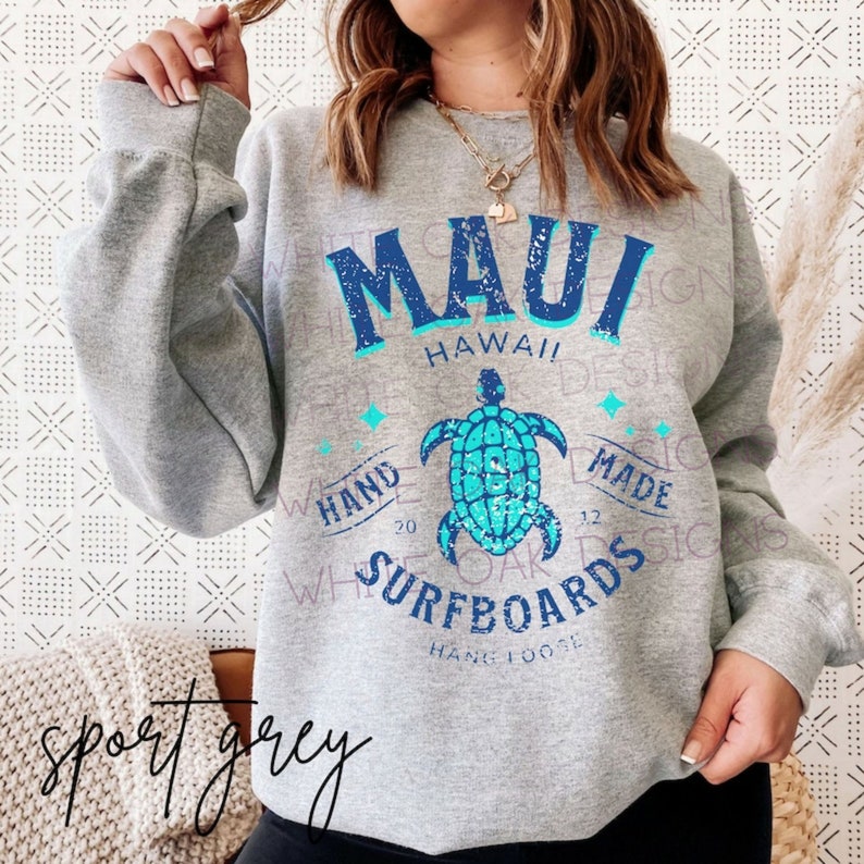 May include: A gray sweatshirt with a blue and turquoise graphic design featuring a turtle and the text "Maui Hawaii Hand Made Surfboards".