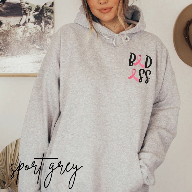 May include: A gray hooded sweatshirt with the text "BAD ASS" in black lettering and pink ribbon designs.