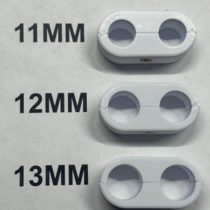 K&ouml;nnte beinhalten: Drei wei&szlig;e Kunststoff-Kabelklemmen mit jeweils zwei L&ouml;chern. Die Klemmen sind mit 11 mm, 12 mm und 13 mm beschriftet.
