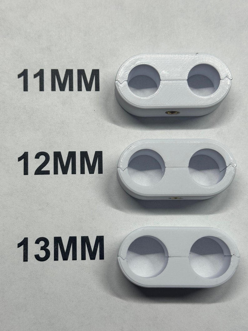 K&ouml;nnte beinhalten: Drei wei&szlig;e Kunststoff-Kabelklemmen mit jeweils zwei L&ouml;chern. Die Klemmen sind mit 11 mm, 12 mm und 13 mm beschriftet.