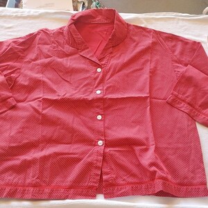 Könnte beinhalten: Rotes Pyjama-Oberteil mit weißen Punkten. Das Oberteil hat einen Kragen, lange Ärmel und eine Knopfleiste mit weißen Knöpfen. Der Saum und die Manschetten sind mit einem roten Rand versehen. Der Stoff scheint leicht zu sein.