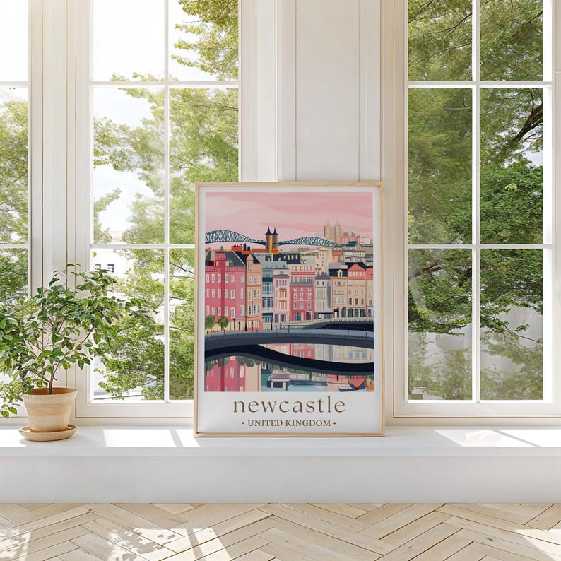 A framed poster of Newcastle, United Kingdom, displayed on a window sill with a potted plant to the left.