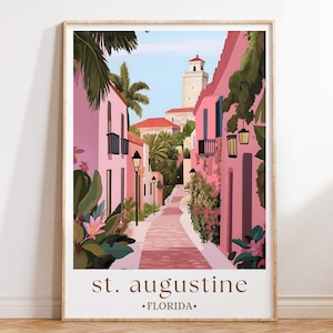 Könnte beinhalten: Gerahmter Kunstdruck einer Straßenszene in St. Augustine, Florida. Die Illustration zeigt rosafarbene Gebäude, eine Backsteinstraße und einen hohen weißen Turm. Palmen und Grün verleihen ein tropisches Flair. Der Text "st. augustine - FLORIDA" befindet sich unten.