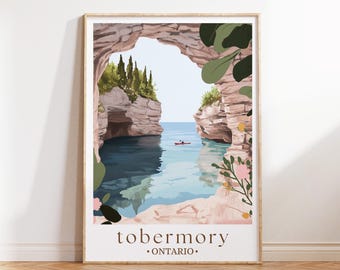 May include: A framed art print featuring a scenic view of Tobermory, Ontario. The illustration depicts a natural rock archway overlooking a calm blue sea with a kayak. The artwork includes floral and foliage accents, with the town name at the bottom.