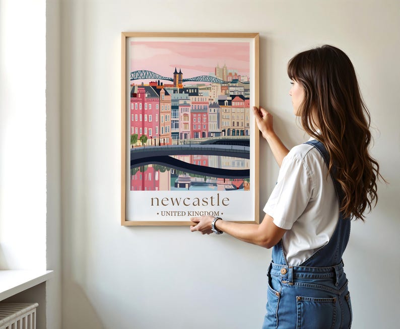 A woman is hanging a framed poster of Newcastle, United Kingdom, on a wall.