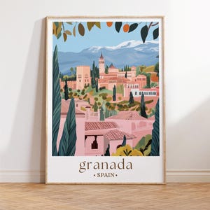 Könnte beinhalten: Ein gerahmter Kunstdruck mit einer farbenfrohen Illustration von Granada, Spanien. Das Kunstwerk zeigt ein Stadtbild mit rosa Gebäuden, grünen Bäumen und schneebedeckten Bergen unter blauem Himmel. Das Wort "granada" ist unten aufgedruckt.