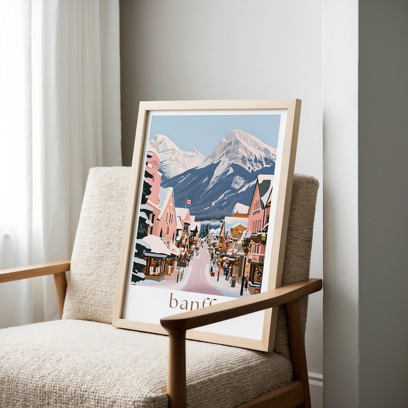 A framed illustration of a snowy mountain town with colorful buildings and a winding road, displayed on a chair in a room with white walls.