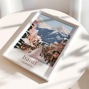 A framed poster of a snowy mountain town in Alberta, Canada, with colorful buildings and a ski lift.