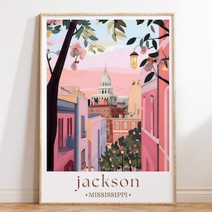 Op de afbeelding: Een ingelijste kunstdruk met een kleurrijke illustratie van Jackson, Mississippi. Het kunstwerk toont een straatbeeld met gebouwen in roze, perzik en blauw, met een gebouw met een koepel op de achtergrond. De tekst "jackson • MISSISSIPPI •" staat onderaan.