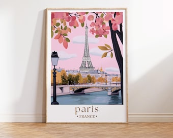 May include: A framed art print featuring a colorful illustration of Paris, France. The Eiffel Tower is the focal point, set against a pink sky, with a bridge and buildings in the background. Pink blossoms and a black tree branch frame the scene. The word "paris" is at the bottom.