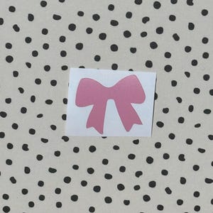 Puede incluir: Una pegatina de lazo rosa sobre un fondo blanco con lunares negros.