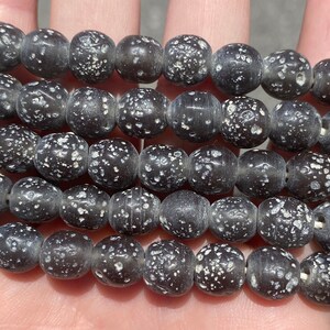 May include: A strand of black glass beads with white speckles. The beads are round and have a matte finish.