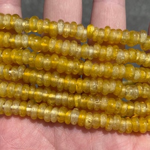 May include: A strand of yellow glass beads with a bubbly texture. The beads are round and have a translucent appearance.