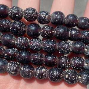 May include: A strand of dark brown beads with white speckles. The beads are round and have a slightly textured surface.