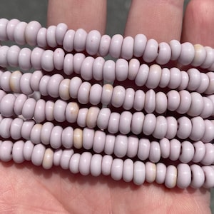 May include: A strand of light purple glass beads. The beads are small and round, and they are strung together on a clear thread.