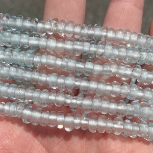 May include: A strand of light blue glass beads. The beads are small and round, and they have a slightly frosted finish.