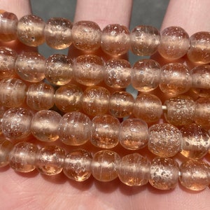 Op de afbeelding: Een streng doorschijnende perzikkleurige glazen kralen met een gespikkelde, bubbelige textuur.