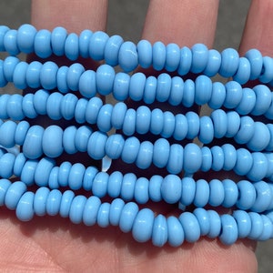 May include: A strand of light blue glass beads. The beads are small and round, and they have a smooth, polished finish.