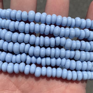 May include: A close-up of a strand of light blue glass beads. The beads are small and round, and they are arranged in a row.