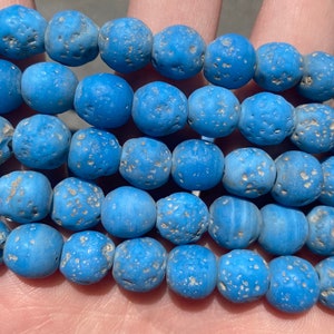 May include: A strand of blue glass beads with a speckled texture. The beads are round and have a matte finish.