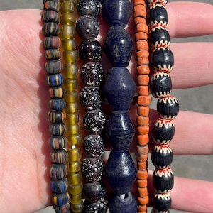 May include: A collection of beaded bracelets in various colors. The bracelets feature beads in shades of orange, yellow, blue, black, and white. The beads have different shapes and patterns, including stripes, speckles, and geometric designs.