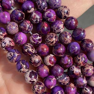 May include: A strand of purple and white jasper beads. The beads are round and have a speckled pattern.