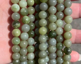 May include: A collection of smooth, spherical beads in various shades of green, ranging from pale mint to deep olive and greyish-green. The beads are arranged in multiple vertical strands, showcasing a polished, semi-translucent finish.
