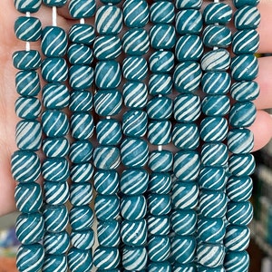 May include: A strand of teal blue and white striped glass beads. The beads are round and have a swirl pattern.