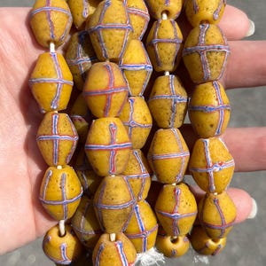Peut inclure: Un chapelet de perles de verre jaunes ornées de motifs croisés rouges et bleus. Les perles sont enfilées sur une ficelle blanche. Les perles de forme ovale sont probablement vintage ou antiques.
