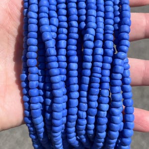 May include: Multiple strands of small, round, matte blue beads arranged in a vertical, parallel formation. Each individual bead features a consistent, opaque cobalt blue colour with a slightly irregular, organic shape and a smooth, non-reflective finish.