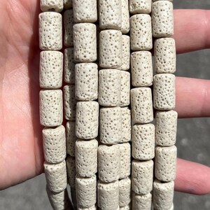 Può includere: Una collezione di perline cilindriche con una consistenza porosa color bianco sporco. Ogni perlina presenta una superficie ruvida e coerente con numerose piccole rientranze, disposte in più fili verticali per mostrare la forma uniforme.