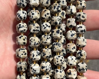 May include: A collection of faceted dalmatian jasper beads strung on thin gold-toned wire. Each bead features a cream-coloured base with distinct black spots. The beads are arranged in multiple vertical rows, showcasing a uniform geometric shape.