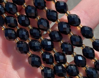 May include: A strand of black faceted glass beads with gold accents. The beads are oval shaped and have a shiny finish.
