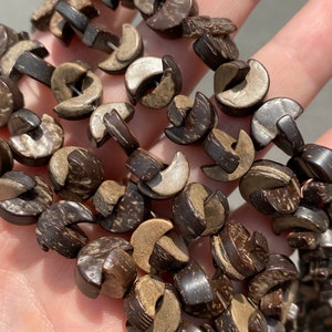 May include: A strand of brown and beige coconut shell beads. The beads are shaped like half circles and are strung together to form a necklace or bracelet.