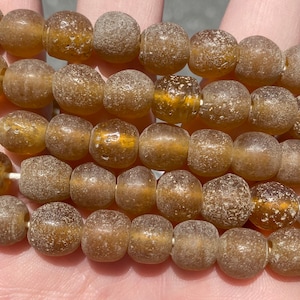 May include: A strand of brown glass beads with a textured surface. The beads are round and have a slightly irregular shape.