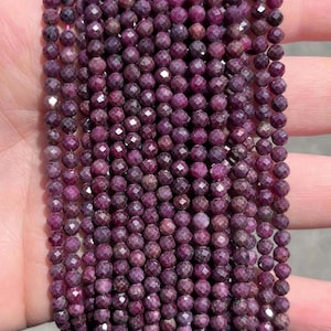 Peut inclure: Un collier de petites perles de rubis rondes et facettées dans des tons magenta profond et violet foncé. Les perles sont uniformes en taille et en forme, avec une surface réfléchissante à facettes multiples, disposées en rangées parallèles.