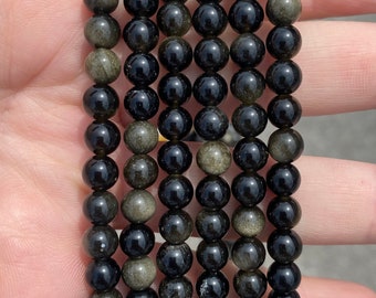 May include: A set of seven black and gold beaded bracelets. The beads are round and have a shiny finish. The bracelets are stacked on top of each other.