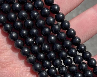 Op de afbeelding: Een streng zwarte obsidianen kralen, elke kraal is rond en glad. De kralen zijn aan elkaar geregen op een doorzichtige draad.