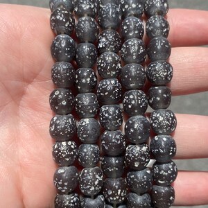May include: A strand of black and white speckled round beads. The beads are made of glass and have a matte finish.