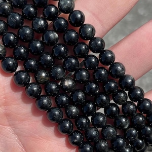 May include: A strand of black obsidian beads with a shimmering, iridescent effect. The beads are round and smooth, and they are strung together on a clear elastic cord.