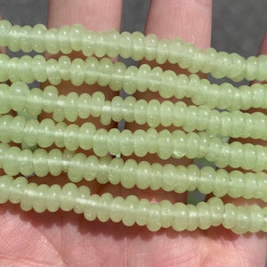 May include: A strand of light green glass beads with a textured surface. The beads are round and have a slightly irregular shape.