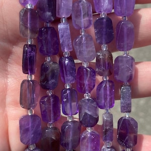 May include: A strand of purple amethyst gemstone beads. The beads are faceted and have a rectangular shape. The beads are strung on silver wire.