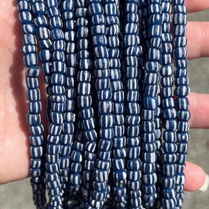 May include: A collection of multiple strands of small, cylindrical beads featuring a deep navy blue base colour with vertical white stripes running along the length of each bead. The beads are arranged in parallel rows, creating a uniform pattern.