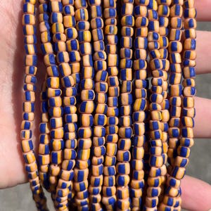 May include: Multiple strands of small, cylindrical beads arranged in vertical rows. Each individual bead features a distinct color pattern consisting of alternating vertical stripes of bright orange and deep blue, creating a uniform appearance.