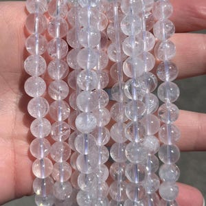 May include: A collection of clear quartz crystal bead bracelets. Each bracelet features round, translucent beads. The beads are approximately 0.8 cm in diameter. The bracelets are held together, highlighting their delicate construction and natural beauty.